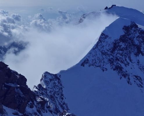 Wir schauen hinunter in den Grenzsattel. Rechts schließt die Zumsteinspitze an, im Hintergrund sieht man die Punta Margherita mit der gleichnamigen Hütte am Gipfel.
